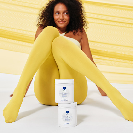 A model sitting down posing with two jars of Fertility Support stacked on top of each other in front of her legs.