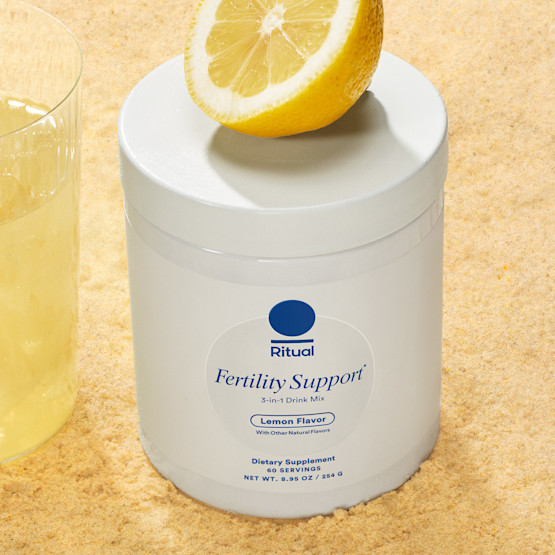 Jar of Ritual's Fertility Support with a half lemon positioned on top and a glass of the mixed product to the left.
