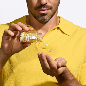 Male in yellow shirt pouring bottle of Essential for Men 18+ into his hand.
