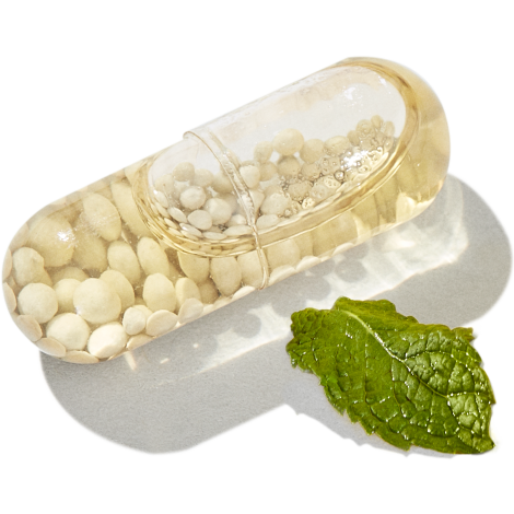 Close up shot of singular multivitamin capsule next to a mint leaf